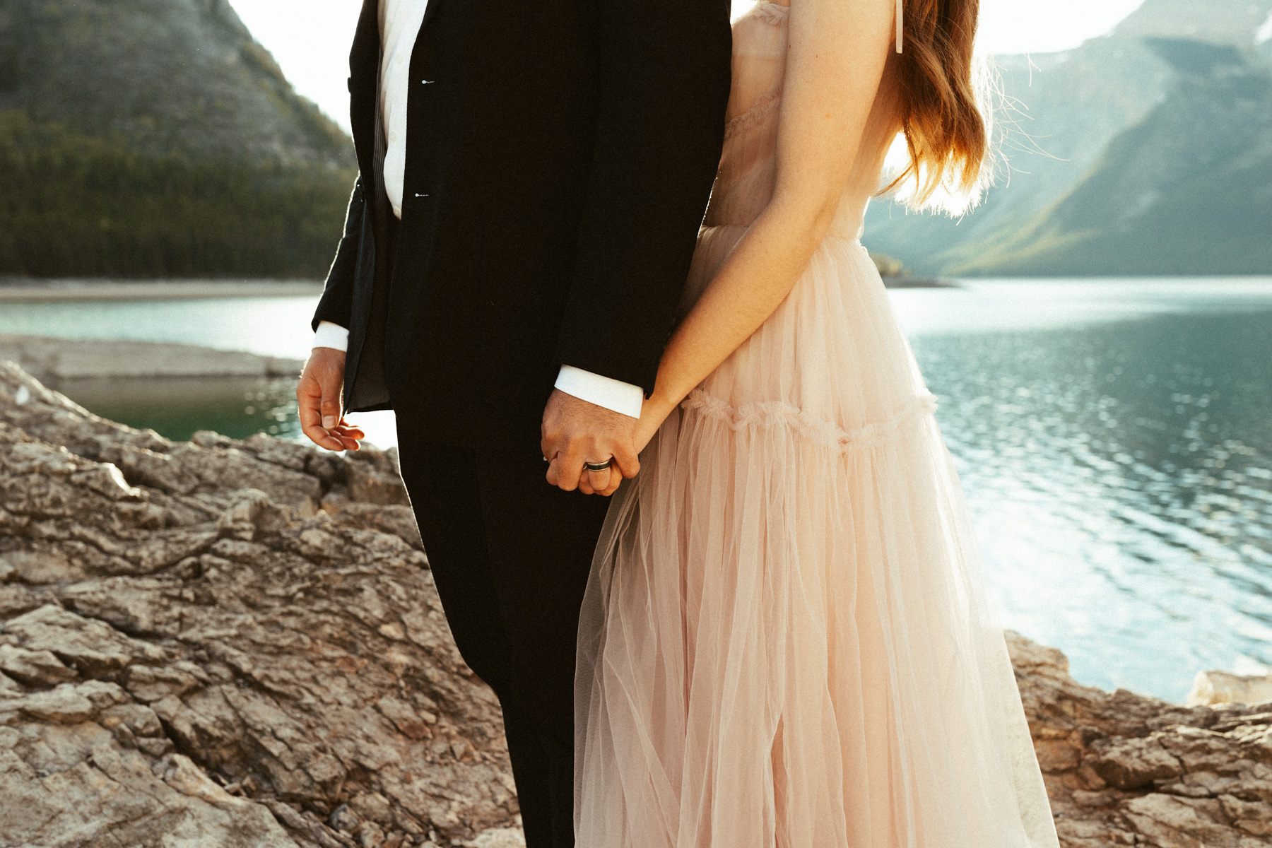 bride and groom holding hands in front of lake minnewanka